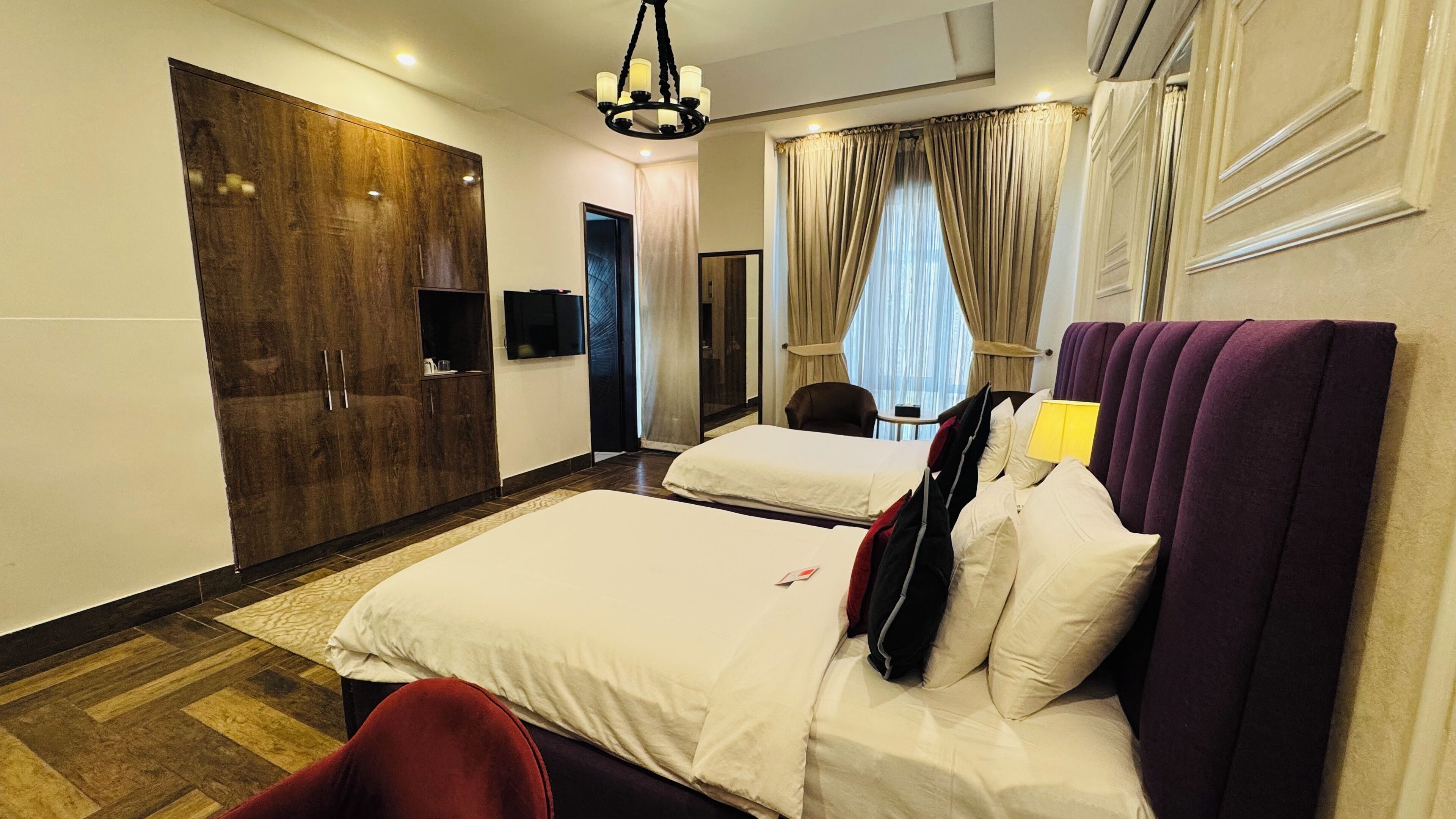 A hotel room with two beds, a wardrobe, a TV, and a chandelier.