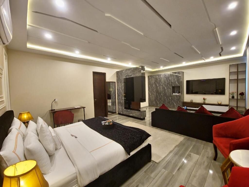Una habitación de hotel moderna con una cama grande, un área de descanso con sillas rojas, un televisor montado en la pared y una pared de acento de mármol.
