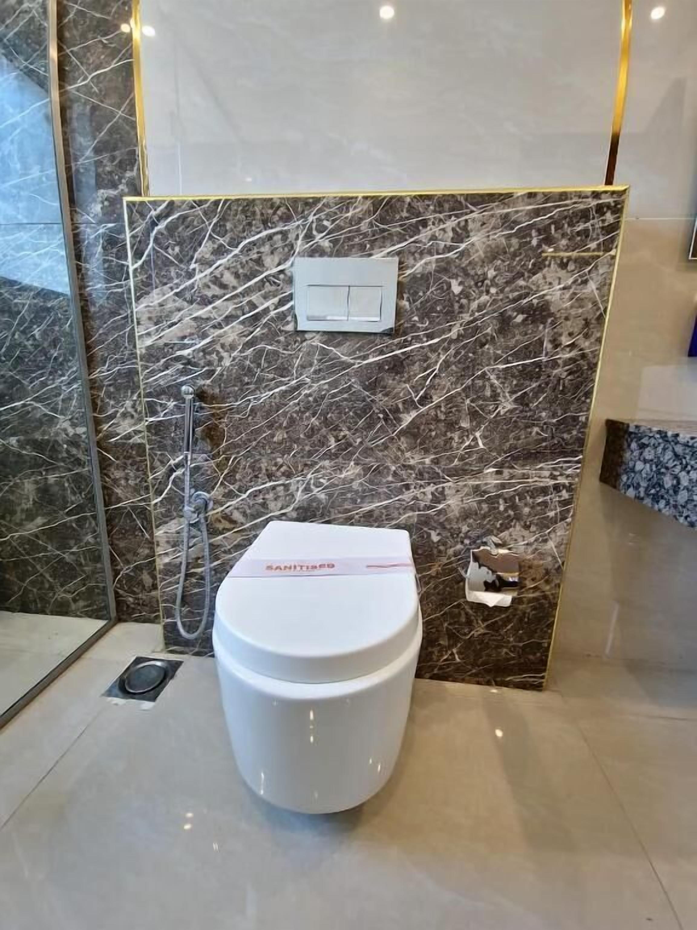 A bathroom with a marble wall, a white toilet, and a shower.