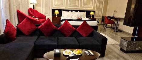 A hotel room with a bed, a sofa with red cushions, a coffee table with breakfast items, and a TV.