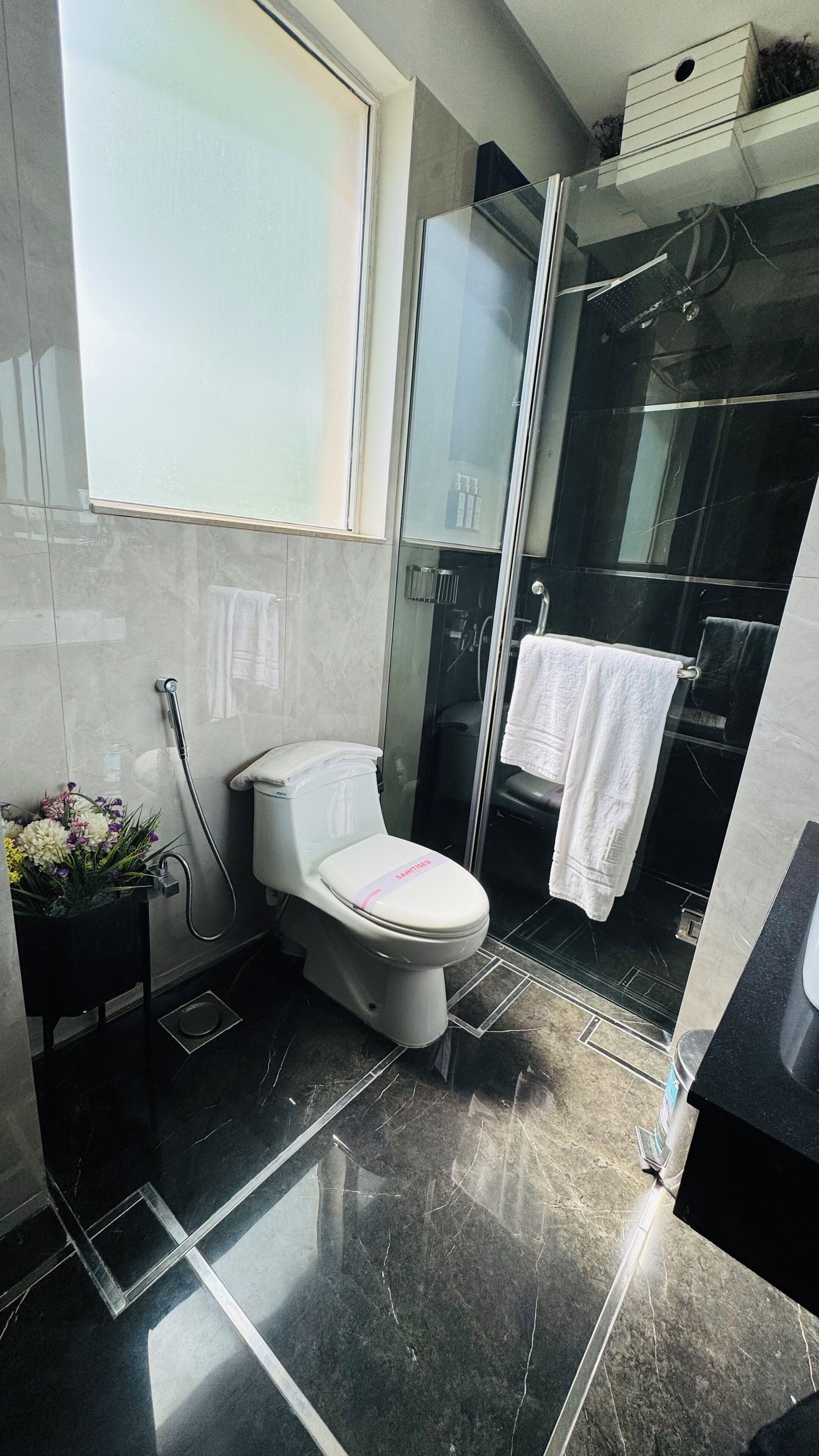 A modern bathroom with a toilet, a glass shower enclosure, and a window.