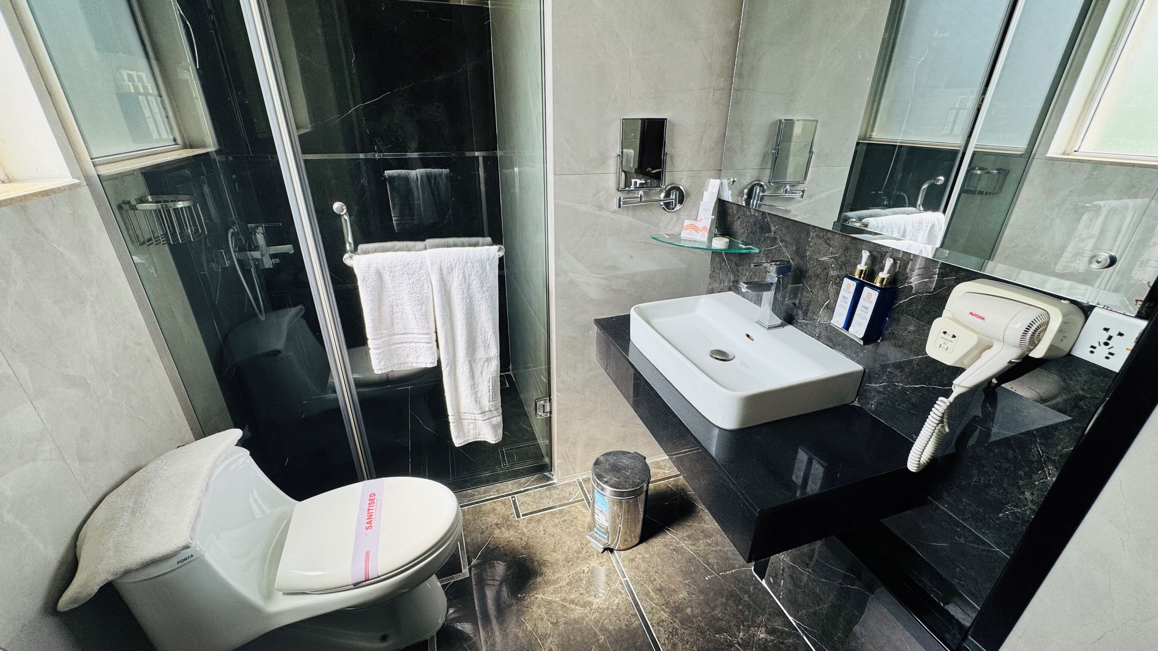 A modern bathroom with a glass shower enclosure, a white toilet, a sink with a black countertop, and a mirror above the sink.