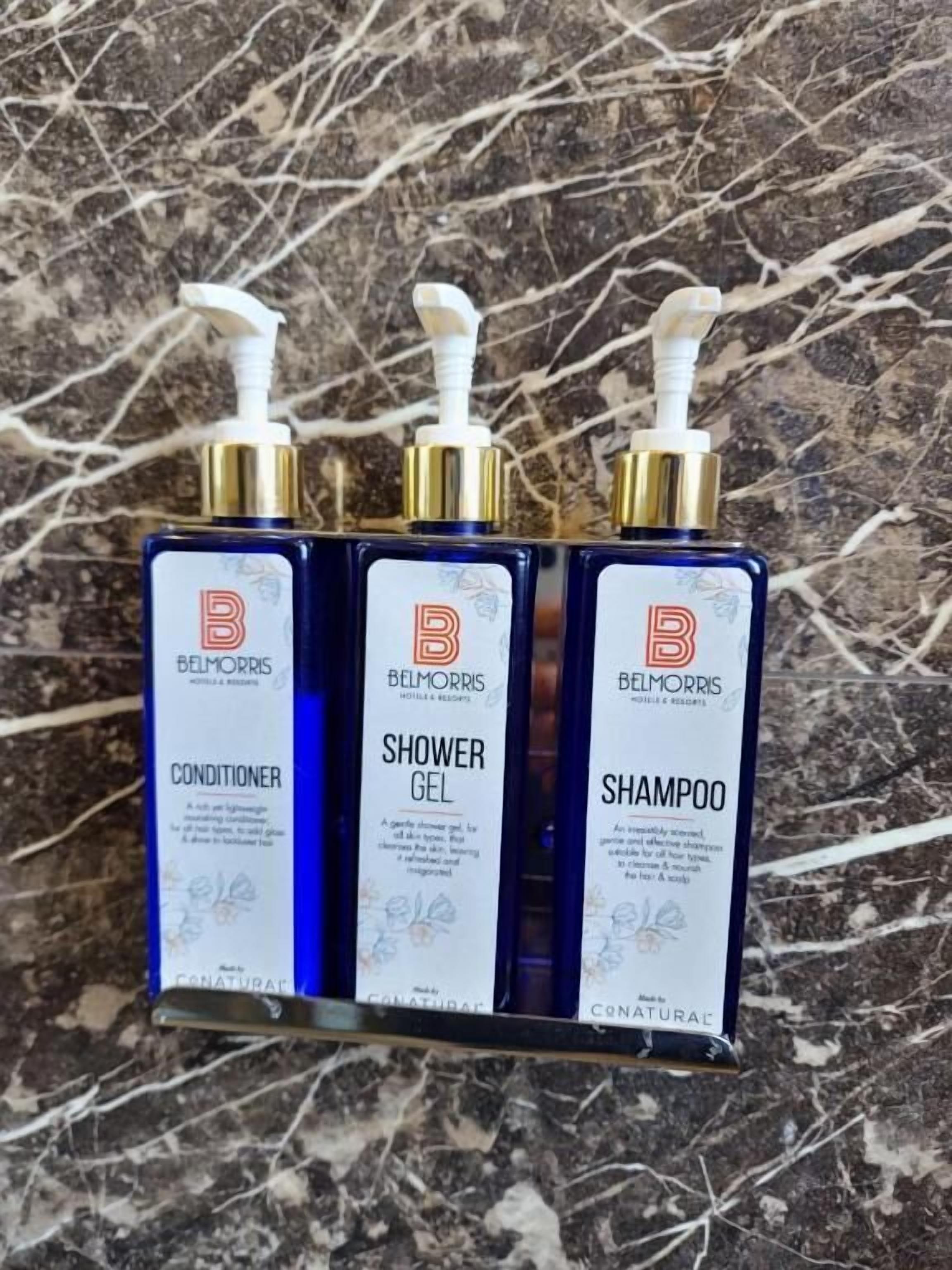 Tres botellas de productos Belmorris: acondicionador, gel de ducha y champú, dispuestas sobre una superficie de mármol.