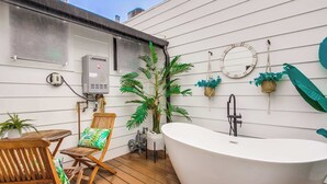 Une salle de bain avec une baignoire sur pieds, une terrasse en bois et des plantes en pot.