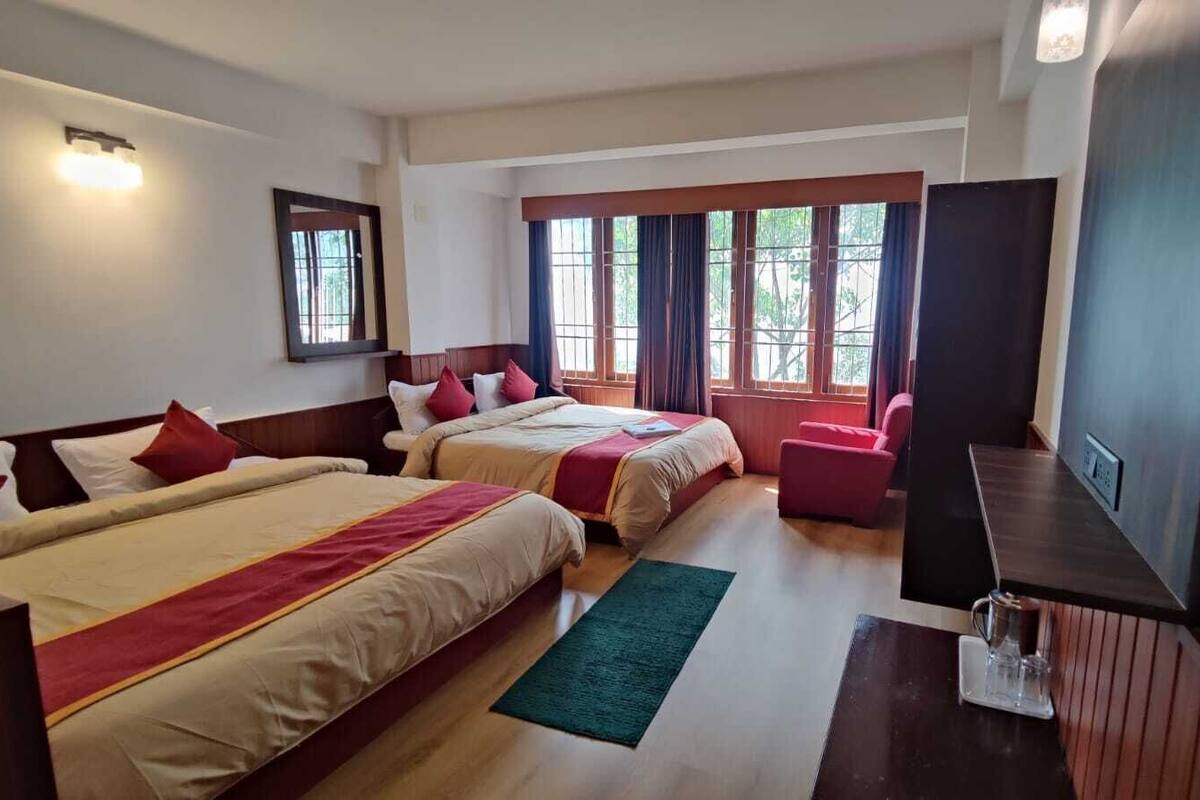 A hotel room with two beds, a TV, a desk, and a window with curtains.