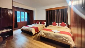 A hotel room with two beds, wooden flooring, a wardrobe, and a large window.