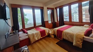 A hotel room with two beds, large windows, a desk, and a television.