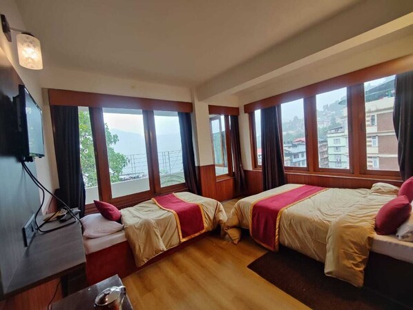 A hotel room with two beds, large windows, a desk, and a television.