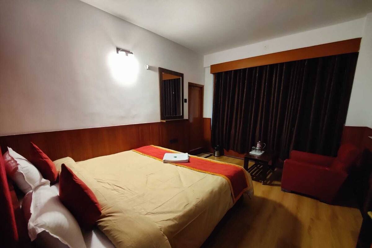 A hotel room with a large bed, a desk, a chair, and a window with curtains.