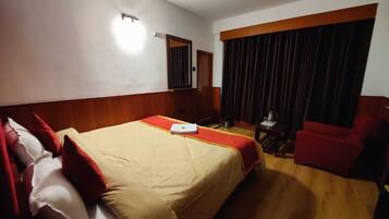 A hotel room with a large bed, a desk, a chair, and a window with curtains.