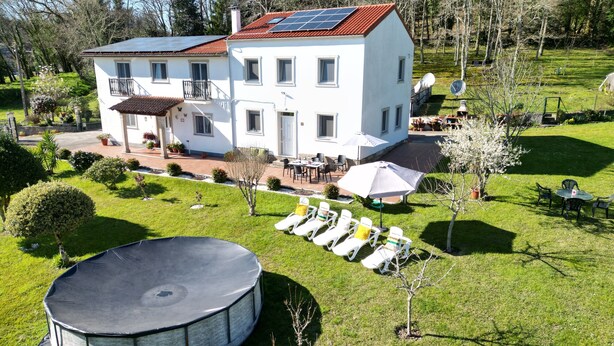 A white two-story house with a solar panel roof, a patio with outdoor furniture, and a trampoline in the foreground.
