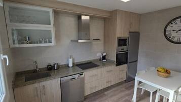 A modern kitchen with a dishwasher, stainless steel appliances, a clock, and a dining area with a table and chairs.