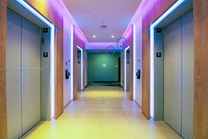 A modern hallway with elevators, marked with floor numbers, and illuminated by neon lights. - Private terrace above the Miami skyline: 1BR corner unit, 25th floor, Downtown Miami (Miami)