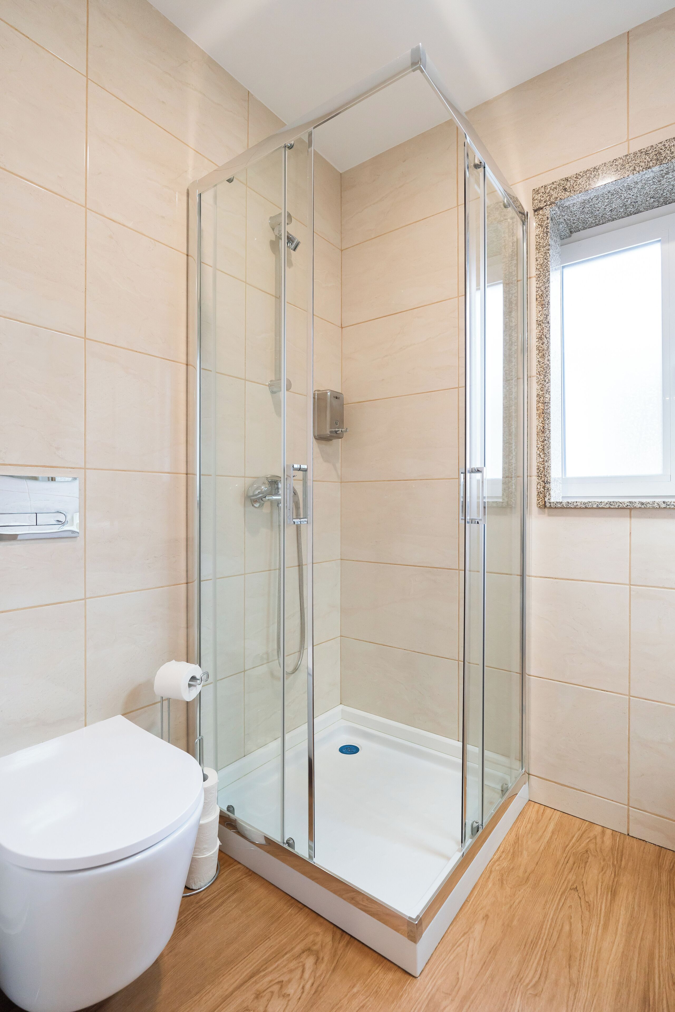 A modern bathroom with a glass-enclosed shower, a white toilet, and a wooden floor.