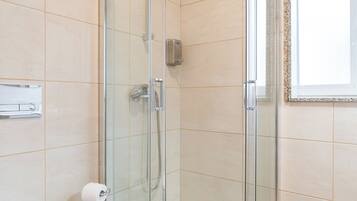 A modern bathroom with a glass-enclosed shower, a white toilet, and a wooden floor.
