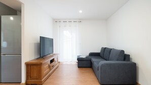 Ein modernes Wohnzimmer mit einem grauen Sofa, einer Holztrenneinrichtung mit Flachbildfernseher und einer Küchenzeile inklusive Kühlschrank.