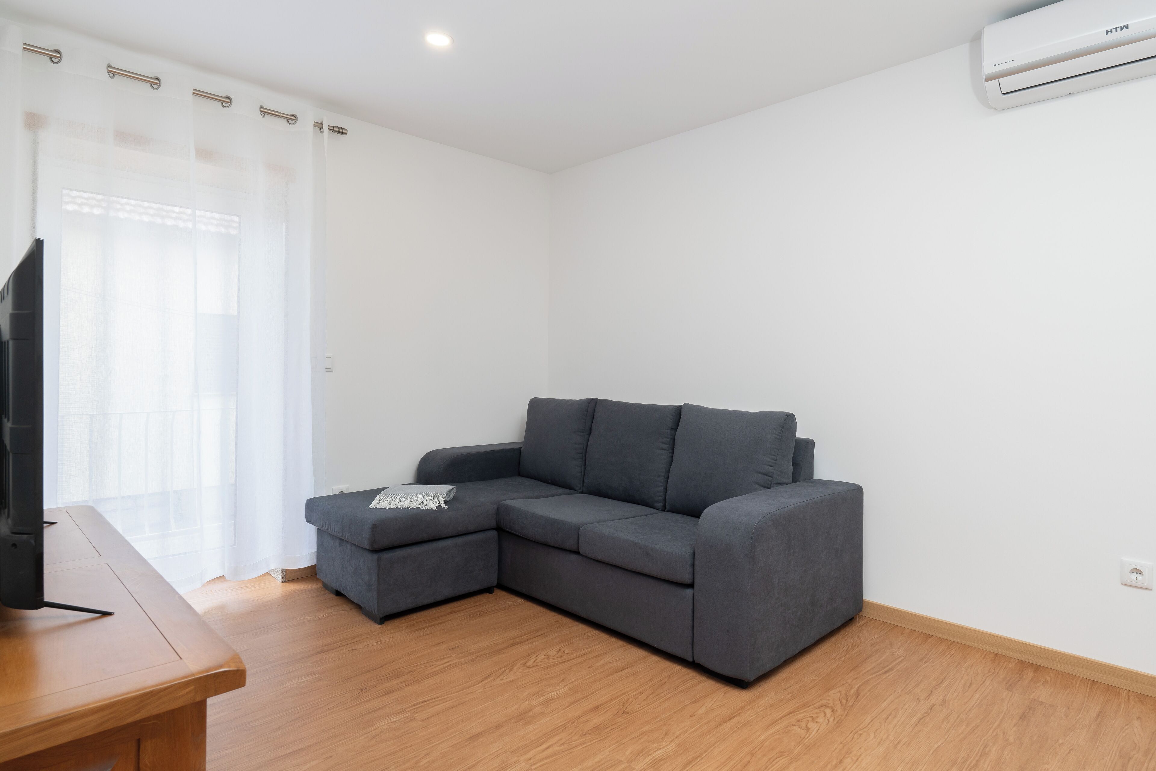 Un salon moderne avec un canapé d’angle gris, une table basse en bois et un téléviseur à écran plat.