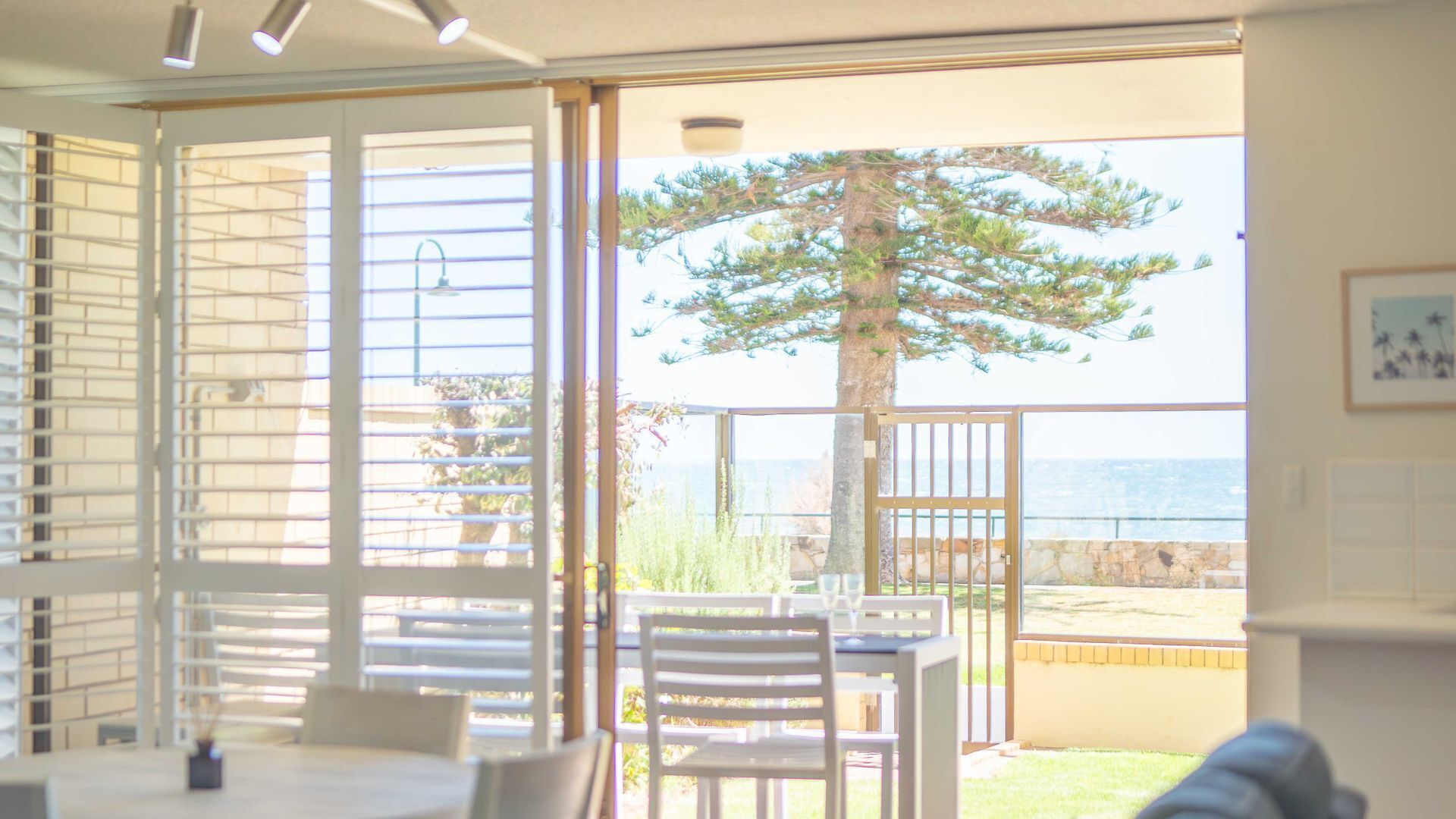 A dining area with a table and chairs, a view of the ocean through a gate, and a tree in the background.