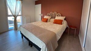 A bedroom with a bed, a nightstand, a window with curtains, and a radiator. - T3 Duplex La Teste, Terrace, Private Parking (La Teste-de-Buch)
