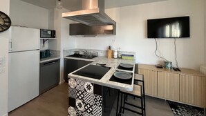 A modern kitchen with a central island, stainless steel appliances, and a flat-screen TV mounted on the wall. - T3 Duplex La Teste, Terrace, Private Parking (La Teste-de-Buch)