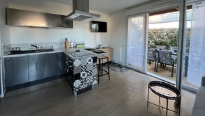 A modern kitchen with a central island, a built-in stove, and a large window overlooking a garden. - T3 Duplex La Teste, Terrace, Private Parking (La Teste-de-Buch)