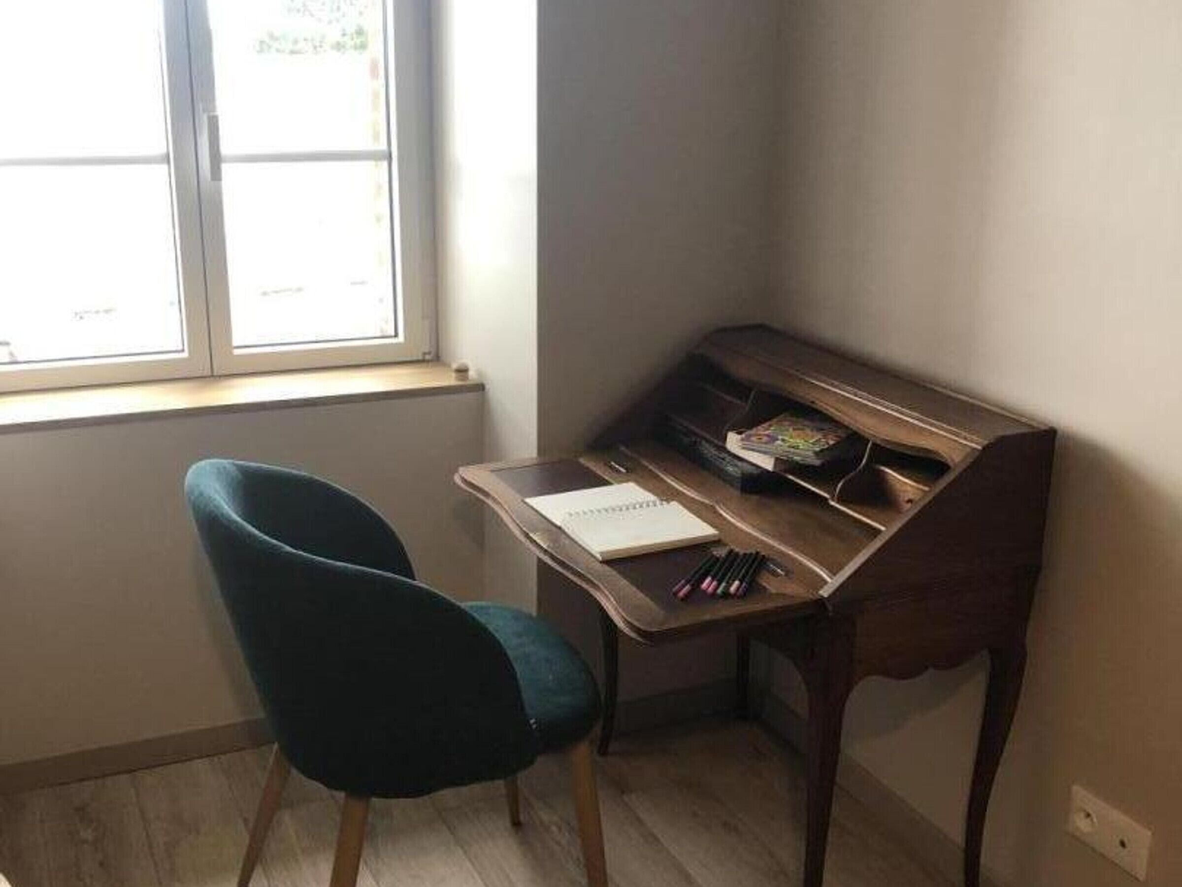 A corner room with a wooden desk, a chair, a window, and a radiator.
