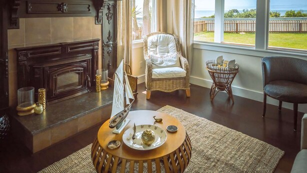 Un salon chaleureux avec une cheminée, un fauteuil en osier et une vue sur l’océan.