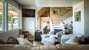 Un salon chaleureux avec une grande fenêtre, un escalier et une vue sur l’extérieur.