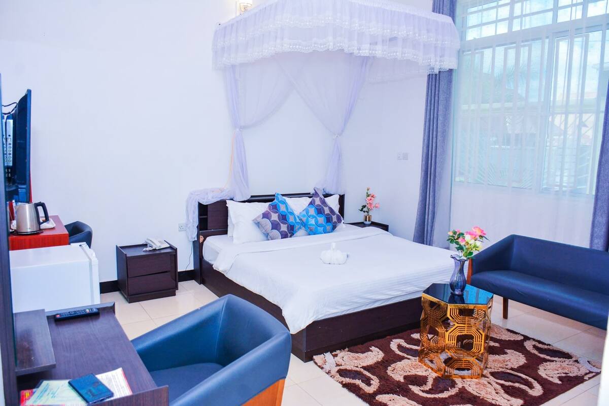 A bedroom with a bed, bedside table, nightstand, and a window with curtains.