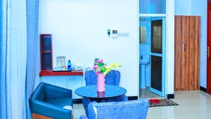 A modern room with a blue sofa, a small round table, and a wooden cabinet. - MARKDON EXECUTIVE LODGE KISASA (Dodoma)