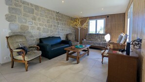 Una sala de estar con paredes de piedra, un sofá verde oscuro, sillones estampados, una mesa de centro de madera y un aparador de madera.