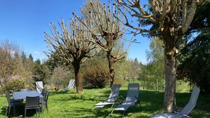 Un espacio al aire libre con mesa y sillas, rodeado de árboles y césped.