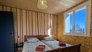 Una cama doble con ropa de cama estampada y dos almohadas, una mesita de noche con una lámpara, una ventana con vistas a árboles y paneles de madera en las paredes.