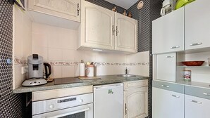 A compact kitchen with white cabinets, a built-in oven, a coffee maker, and a sink. - 2-room apartment 100m from the beach, 4 people (Argelès-sur-Mer)