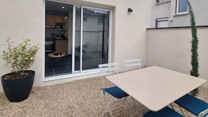 Un pequeño patio con mesa y sillas, una planta en maceta y una puerta corrediza de vidrio que da a una cocina.