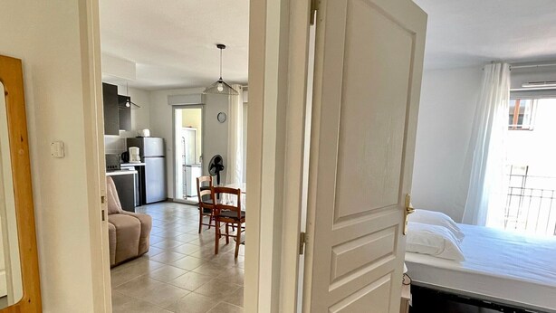 A room with a bed, a dining area with chairs and a table, and a kitchen area with appliances.