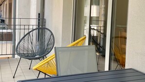A balcony with a chair, a table, and a view of the building's interior.