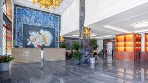 Un vestíbulo con una recepción, un gran mural de peces, columnas de mármol y una moderna araña.