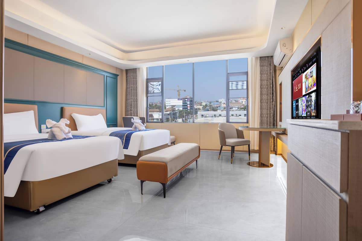A hotel room with two beds, a desk, a chair, and a large window with a city view.