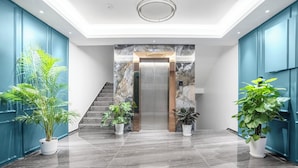 A modern lobby with a marble staircase, a central elevator, and potted plants. - BOLAI BAIJIN HOTEL (Vientiane)