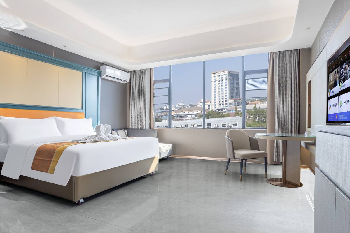 A modern hotel room with a large bed, a desk, and a view of the cityscape.