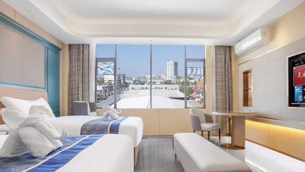 Habitación de hotel con una cama grande, un banco, un escritorio y vistas a la ciudad.