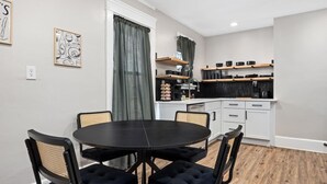 Cocina compacta con armarios blancos, encimera negra y comedor con mesa redonda y cuatro sillas.