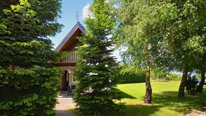 A wooden cabin with a porch, surrounded by lush greenery and a clear sky. - Comfortable Holiday Homes With a Summer Pool (Darlowo)