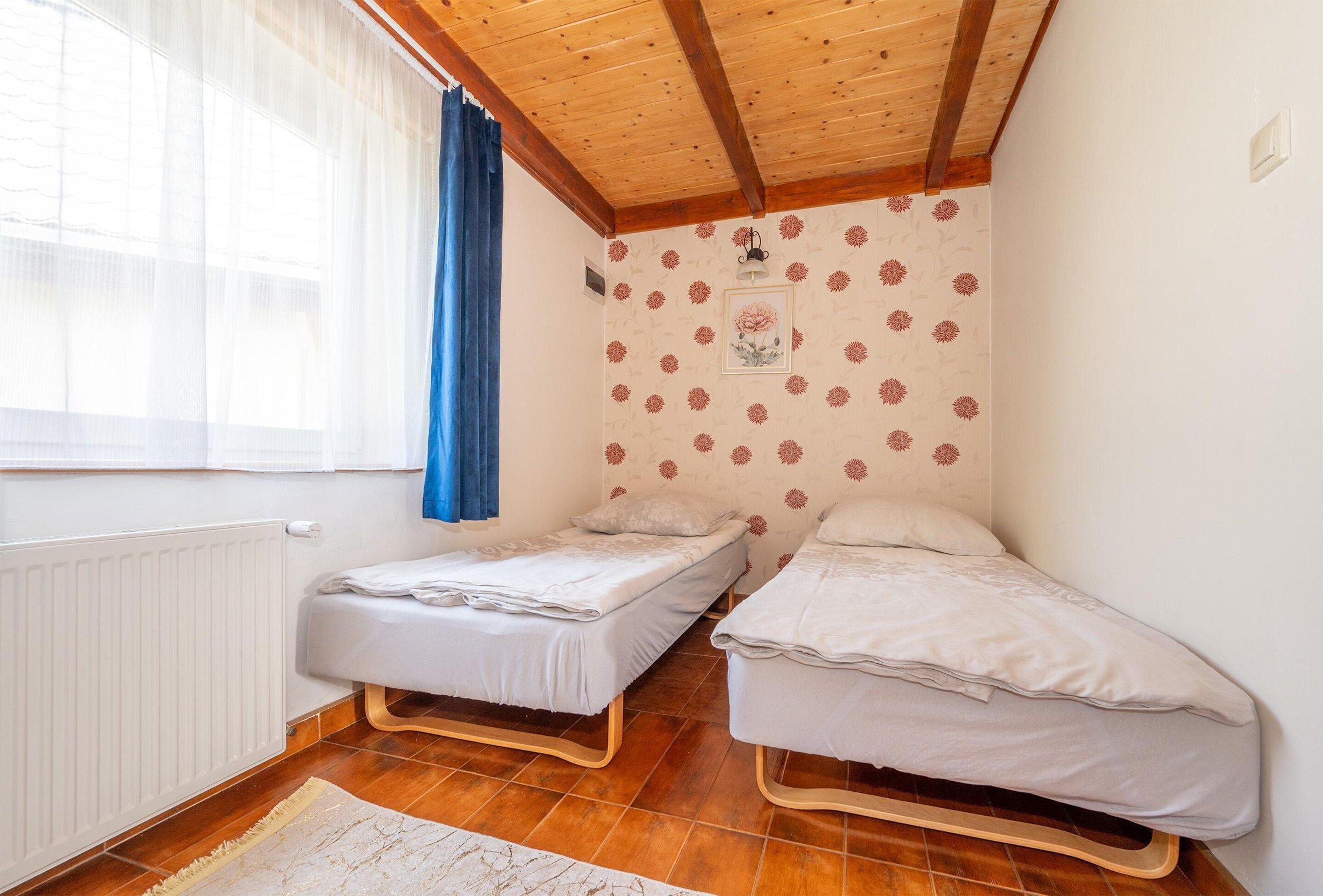 A small room with two single beds, a radiator, a window with curtains, and a patterned wall.