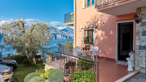 Un balcon avec vue sur la mer et les montagnes, une chaise blanche et des plantes en pot.