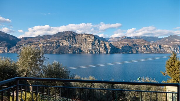 Une vue pittoresque d’un lac, avec des montagnes en arrière-plan, un ciel dégagé et une balustrade de balcon au premier plan.