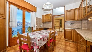 A kitchen with wooden cabinets, a dining table with a checkered tablecloth, and a view of the sea through a sliding door.