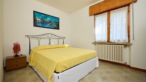 Une chambre à coucher avec un lit, une table de chevet, un radiateur et une fenêtre avec des rideaux.