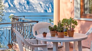 Une table ronde agrémentée de plantes en pot et une chaise blanche sur un balcon donnant sur une étendue d’eau.